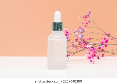 Blank white glass dropper bottle packaging with aromatic oil or serum,water drops,little flowers twig on beige background.Natural organic Spa Cosmetic product design mockup.Front.flat lay,copy space.