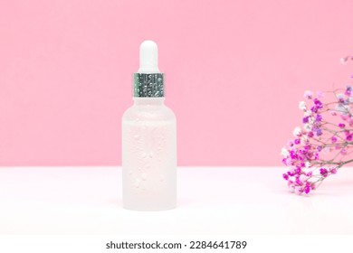 Blank white glass dropper bottle packaging with aromatic oil or serum,water drops,little flowers twig on pink background.Natural organic Spa Cosmetic product design mockup.Front.flat lay,copy space.