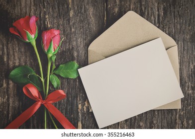 Blank White Greeting Card With Brown Envelope And Red Rose Flowers With Ribbon Bow On Wooden Table With Vintage And Vignette Tone - Valentine And Love Concept