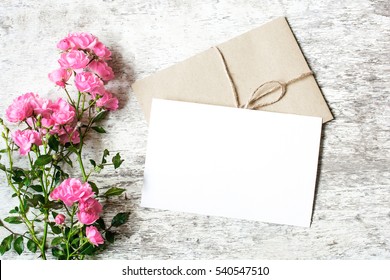 Blank white greeting card and envelope with pink rose flowers mockup on white rustic wood background for creative work design. top view