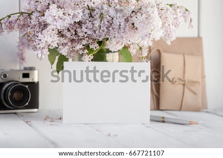 Blank white greeting card with lilac flowers bouquet and envelope with vintage camera on white wooden background. mock up