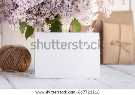 Blank white greeting card with lilac flowers bouquet and envelope on white wooden background. mock up