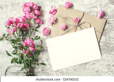 blank white greeting card with pink rose flowers bouquet and envelope with flower buds on white wooden background. vintage toning.top view. mock up - Powered by Shutterstock