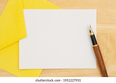 Blank White Greeting Card In Yellow Envelop With A Pen On A Wood Desk