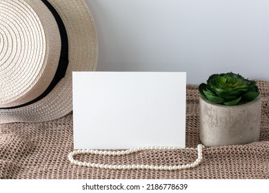 Blank White Invitation Card In Landscape Lay On Knitted Cloth With Beach Hat And Pearl Lace.