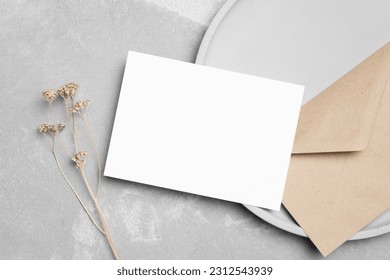 Blank white invitation card mockup with envelopea and dry flowers decor on grey background, top view, copy space