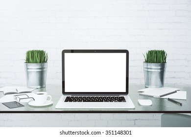 Blank white laptop screen on glassy table with cup of coffee at brick wall background, mock up
