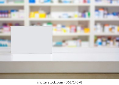 Blank white medicine package on counter with blur shelves of drug in the pharmacy drugstore