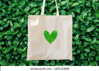 Blank White Mockup Linen Cotton Tote Bag On Green Bush Trees Foliage Background. Heart Logo From Leaves. Nature Friendly Style. Environmental Conservation Recycling Plastic Free Concept