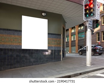 Blank white mockup template for an advertisement board on wall at a street corner. Empty poster background texture at a traffic intersection on the pedestrian sidewalk of an urban road. Copy space.