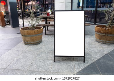 Blank white outdoor advertising stand/sandwich board mock up template. Clear street signage board placed by an outdoor dinning area of a restaurant. Background texture of standee on street. - Shutterstock ID 1572917827