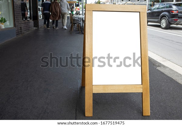 Blank\
white outdoor advertising stand/sandwich board mock up template.\
Clear street signage board with wooden frame placed on pedestrian\
sidewalk. Background texture of standee on\
street.
