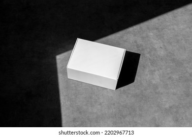 Blank white paper box, packaging mockup, on concrete background, with sharp natural sunlit shadows. Packaging mockup template with empty space to display your branding design. - Shutterstock ID 2202967713
