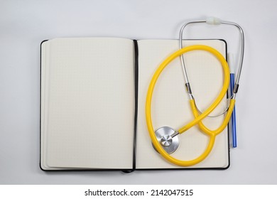 Blank White Paper Notebook With A Blue Ink Pen, Stethoscope, Pen, And Blank Prescription Pad. Medicine Or Pharmacy. Empty Medical Form Ready To Be Used. Modern Medical Information Technology.