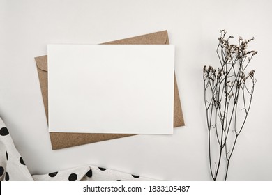 Blank white paper on brown paper envelope with Limonium dry flower and White cloth with black dots. Mock-up of horizontal blank greeting card. Top view of Craft envelope on white background. - Powered by Shutterstock