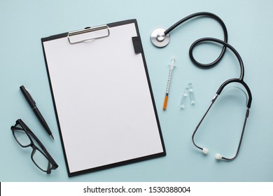 Blank White Paper On Clipboard Near Stethoscope; Injection; Pen And Spectacles Over Blue Desk