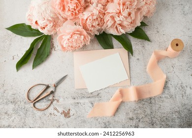 Blank white paper retro post card, coral pink peony flowers and gift ribbon on grunge stone background. Invitation or greeting floral card mockup in vintage style in trendy color 2024 year Peach Fuzz.
