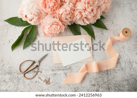 Blank white paper retro post card, coral pink peony flowers and gift ribbon on grunge stone background. Invitation or greeting floral card mockup in vintage style in trendy color 2024 year Peach Fuzz.