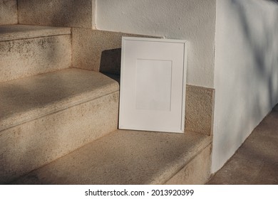 Blank White Picture Frame Leaning Against White Wall. Outdoor Sandstone Stairs In Sunlight, Shadows Overlay. Empty Poster Mockup For Art Display. Minimal Summer Design. No People. 