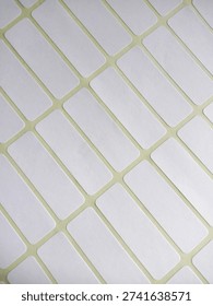 Blank white rectangular adhesive labels arranged diagonally on a yellow backing sheet. These writable stickers are commonly used for pricing, name tags, or organizing office and school supplies.