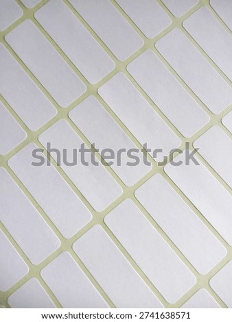 Blank white rectangular adhesive labels arranged diagonally on a yellow backing sheet. These writable stickers are commonly used for pricing, name tags, or organizing office and school supplies.