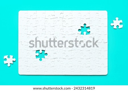 Blank white rectangular puzzle with two final pieces set aside on a serene blue background. Challenge and creativity related concept.