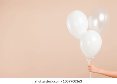 Blank white rubber inflatable balloon holds by human female hand on an abstract beige background. New Year event valentine and birthday celebration concept. Detailed close up studio shot