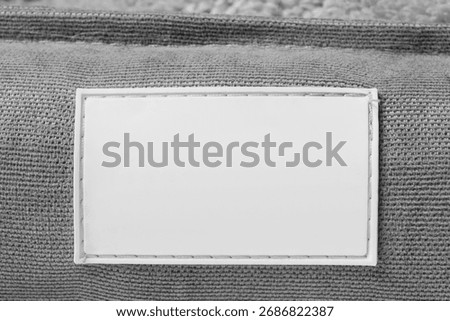 Blank white rubber patch stitched on grey fabric background closeup