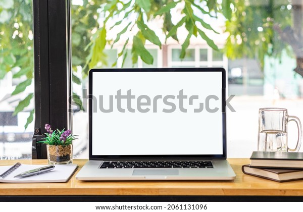 blank white screen laptop and computer screen\
Flower vases of plants and book objects on the table in a coffee\
shop front view beside the\
mirror