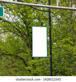 Blank White Sign Attached To A Light Pole With Trees In The Background