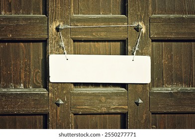 Blank white sign hanged with tattered rope on the old brown wooden door with metal rivets, free space for text, vintage filter processing - Powered by Shutterstock