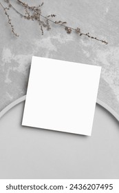 Blank white square card mockup with botanical decor on grey stony background, top view, copy space
