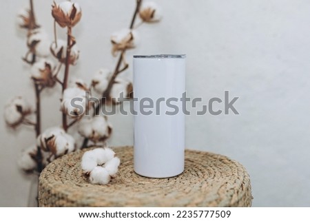 Blank white steel tumbler with cotton flowers background. Mockup white steel tumbler, copy space.