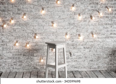 Blank White Stool Against The Backdrop Of A Brick Wall With A Garland Of Light Bulbs