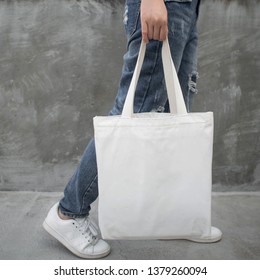 Blank White Tote Bag Canvas Fabric With Handle Mock Up Design. Close Up Of Woman Holding Eco Or Reusable Shopping Bag On Grunge Grey Wall. No Plastic Bag And Ecology Concept.