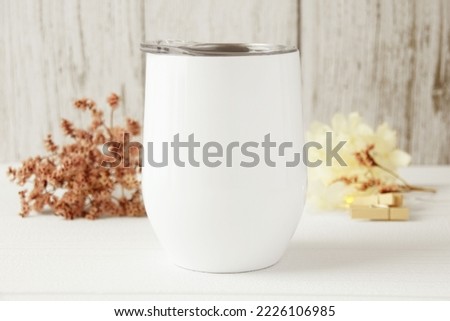 Blank white wine tumbler with lid in white wood background. Fall decor, red and beige flower, wooden clip. Svg product mockup, svg product display, front view, white copy space. 