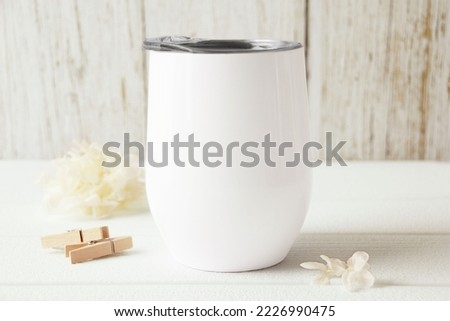 Blank white wine tumbler with lid mockup. Beige flower, wooden clip, white wood background. Svg product mockup, svg product display, mockup for svg product. Front view, white copy space. 