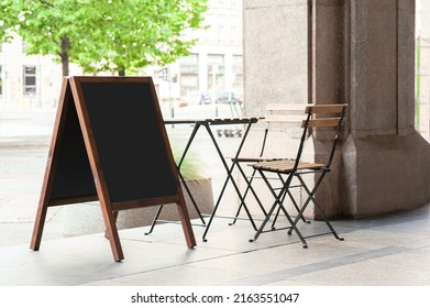 Blank wooden sandwich board near chair and table outdoors. Mockup for design