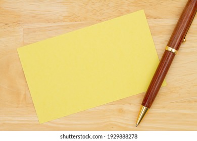 Blank Yellow Paper Index Card With Pen On Wood Desk With Copy Space For Your Message