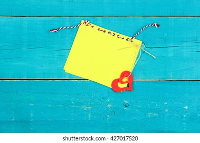 Blank yellow paper note card with red hearts on antique rustic teal blue wood background
