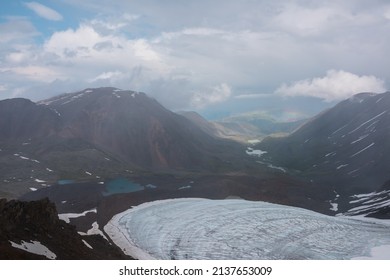 Bleak alpine landscape with rainbow above mountain lake in rain. Top view to  glacier and glacial lake in mountain valley during rain. Gloomy scenery with low clouds in mountains in rainy weather.