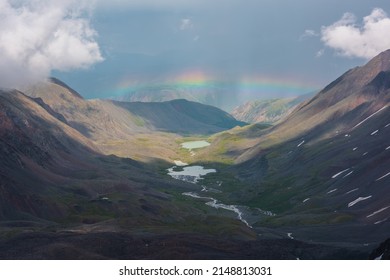 Bleak alpine landscape with vivid rainbow above mountain lake in valley. Gloomy scenery with bright rainbow above lake in mountain valley. Top view to colorful rainbow and low clouds in mountains.