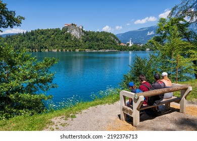 Bled, Slovenia - July 18, 2022: Family Of Four Enjoy Scenic View Of Lake Bled And Bled Castle From A Bench, Popular Tourist Destination.