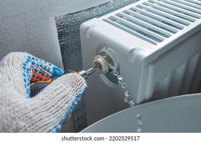 Bleed valve in heating radiator. Hand with a screwdriver draining air for adjusts heating system at home. Preparing the house for the new cold autumn or winter season.