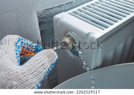 Bleed valve in heating radiator. Hand with a screwdriver draining air for adjusts heating system at home. Preparing the house for the new cold autumn or winter season.