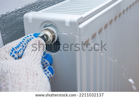 Bleed valve in heating radiator. Hand with a special key for draining air drains water and air from the heater. Adjust heating system, preparing the house for the new cold autumn or winter season.