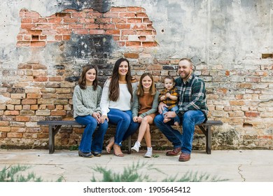 Blended family of five with two girls and a baby boy sitting on a table by an urban old brick wall - Shutterstock ID 1905645412