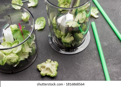 Blender Bowl  With Broccoli. Blender Bowl With Metal Shredder And Broccoli. Green Straws On Table. Black Background. Top View. Close Up
