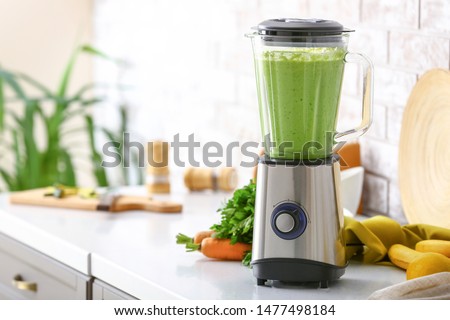 Blender with healthy smoothie and ingredients on table in kitchen