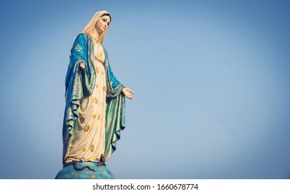 The Blessed Virgin Mary Statue Figure. Catholic Praying For Our Lady - The Virgin Mary. Blue Sky Copy Space On Background